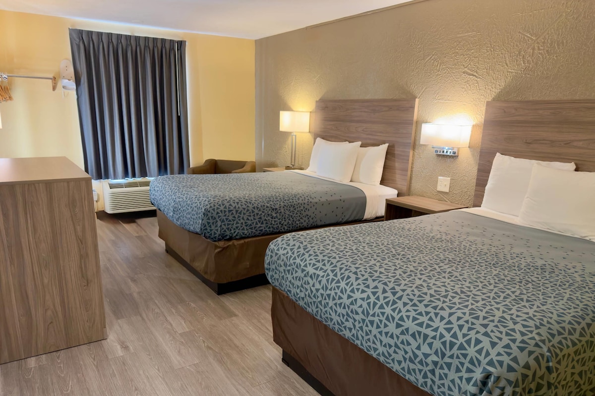 Een hotelkamer met twee bedden, een bureau, een stoel, een wandlamp en een gordijn.