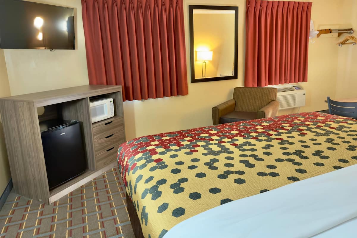 Une chambre d’hôtel comprenant un lit, un bureau avec un micro-ondes, une chaise, une télévision et une fenêtre avec des rideaux.