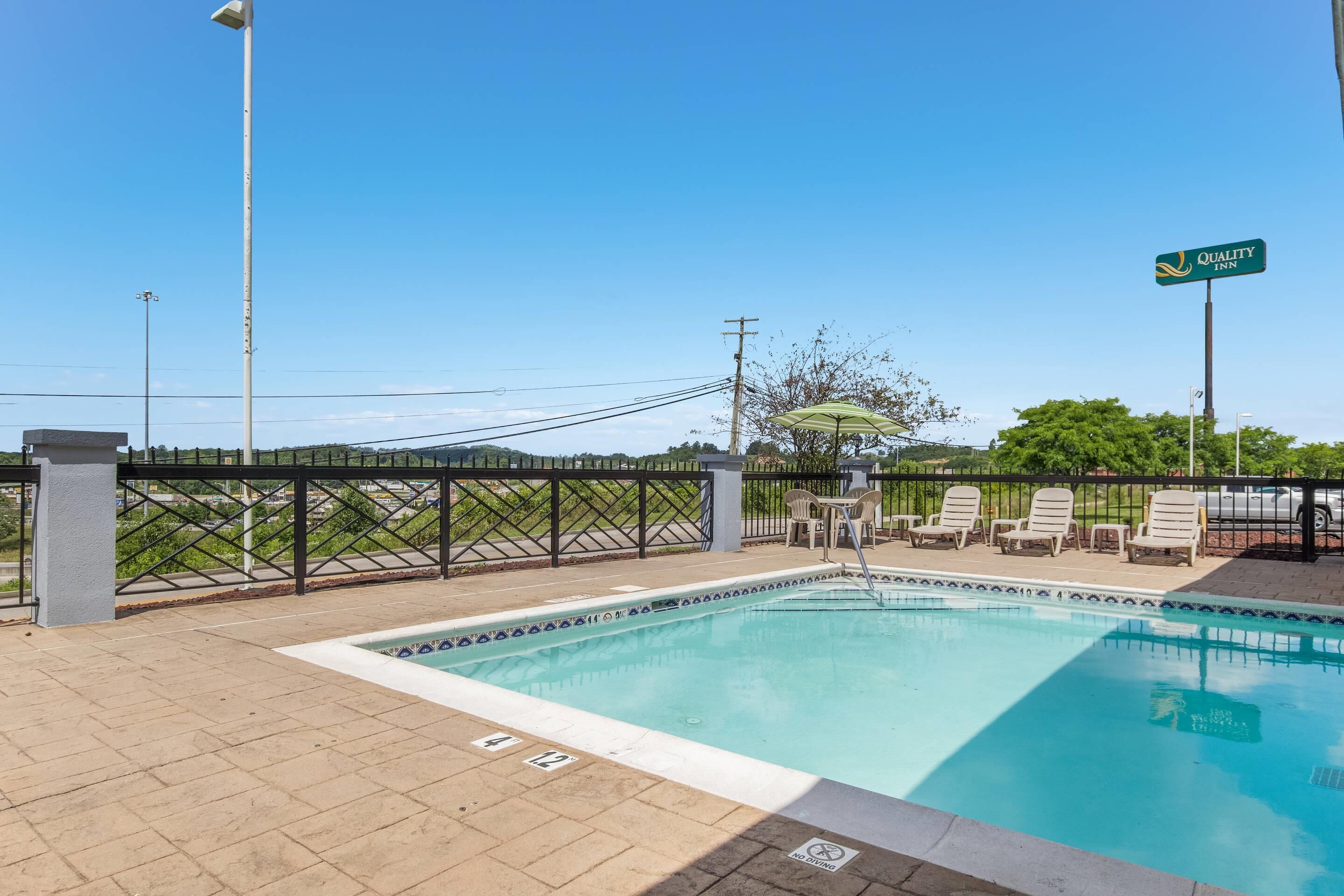 A pool area with lounge chairs, a fence, and a sign for Quality Inn.