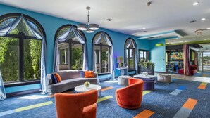 A modern hotel lobby with large arched windows, a gray sofa, orange armchairs, and a colorful carpet. - Quality Inn London North (London)
