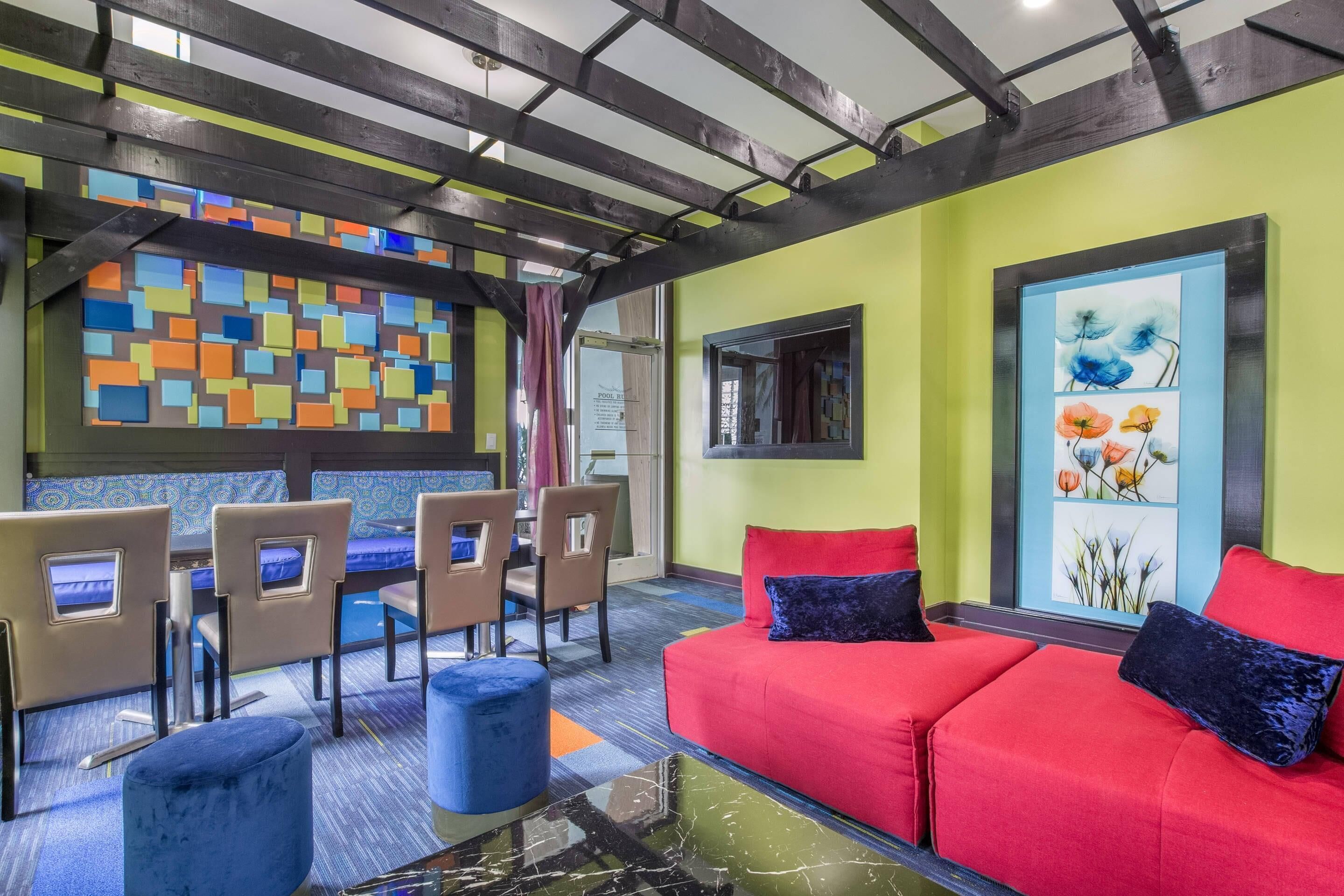 Un intérieur moderne avec un canapé rouge, un pouf bleu et une œuvre d’art abstraite et colorée accrochée au mur.