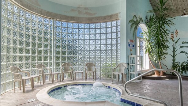A hot tub with a view through a patterned glass wall, surrounded by chairs, and a metal safety railing. - Quality Inn London North (London)