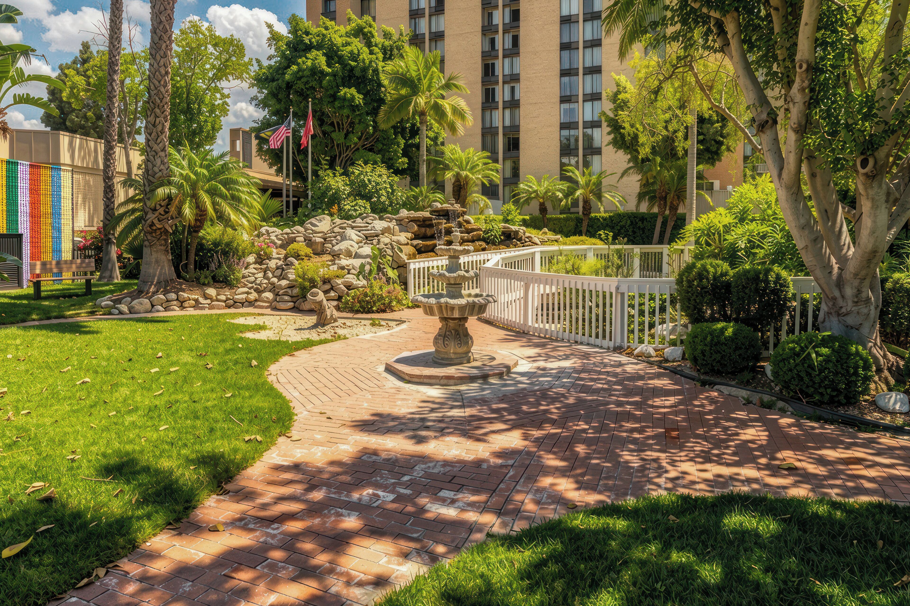 A landscaped garden with a brick pathway, palm trees, and a fountain.
