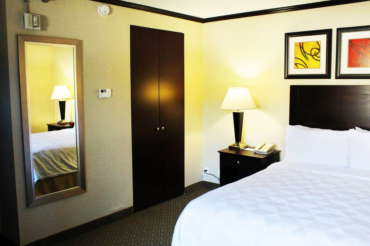 A hotel room with a large bed, a wardrobe, a nightstand with a lamp, and two framed artworks on the wall.