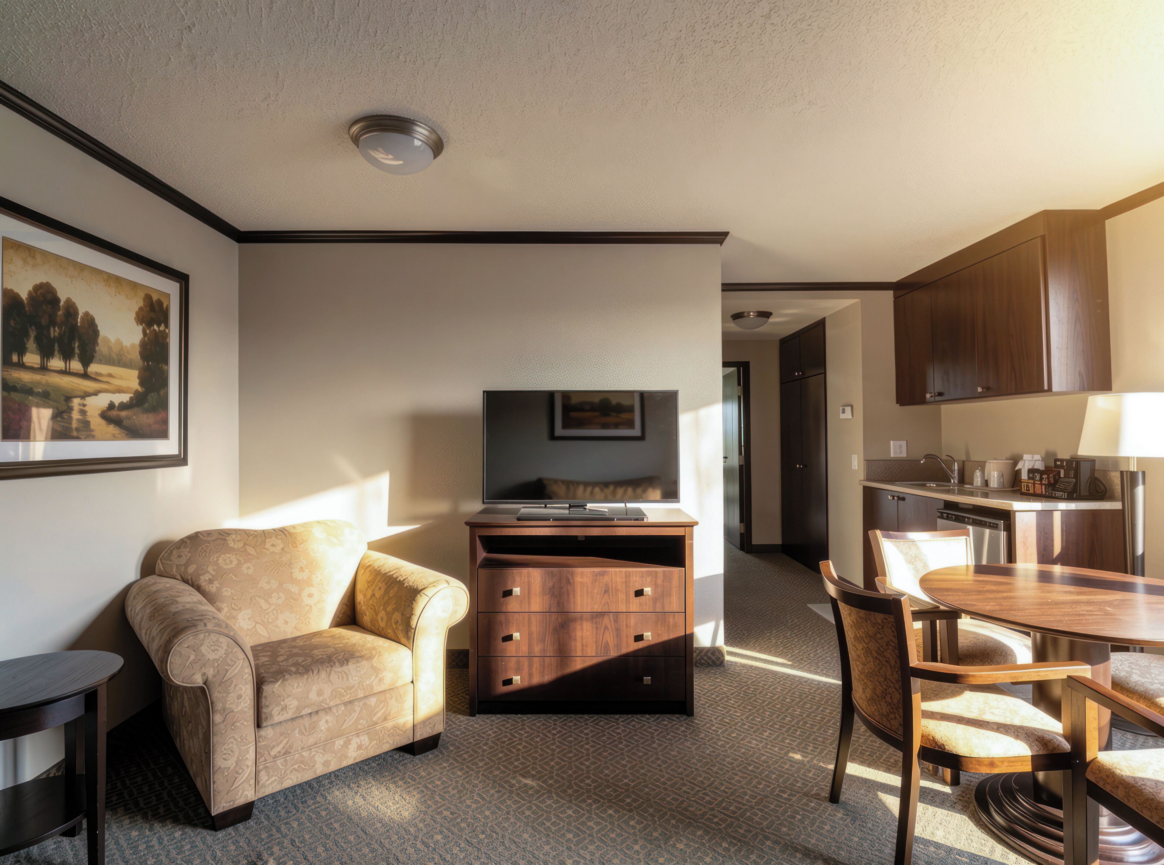 Un espacio habitable compacto con sofá, televisión de pantalla plana, mueble de madera, mesa de comedor con sillas y zona de cocina.