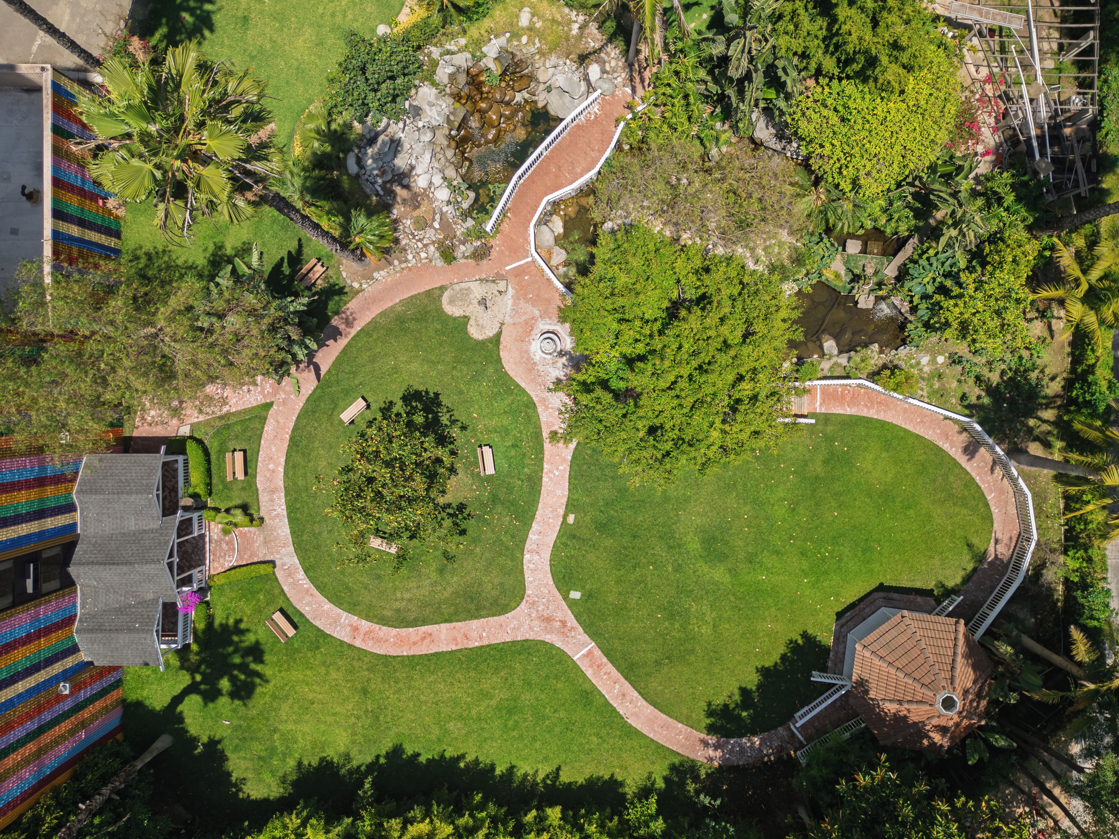 An aerial view of a landscaped area with a circular garden, pathways, and a small pond.