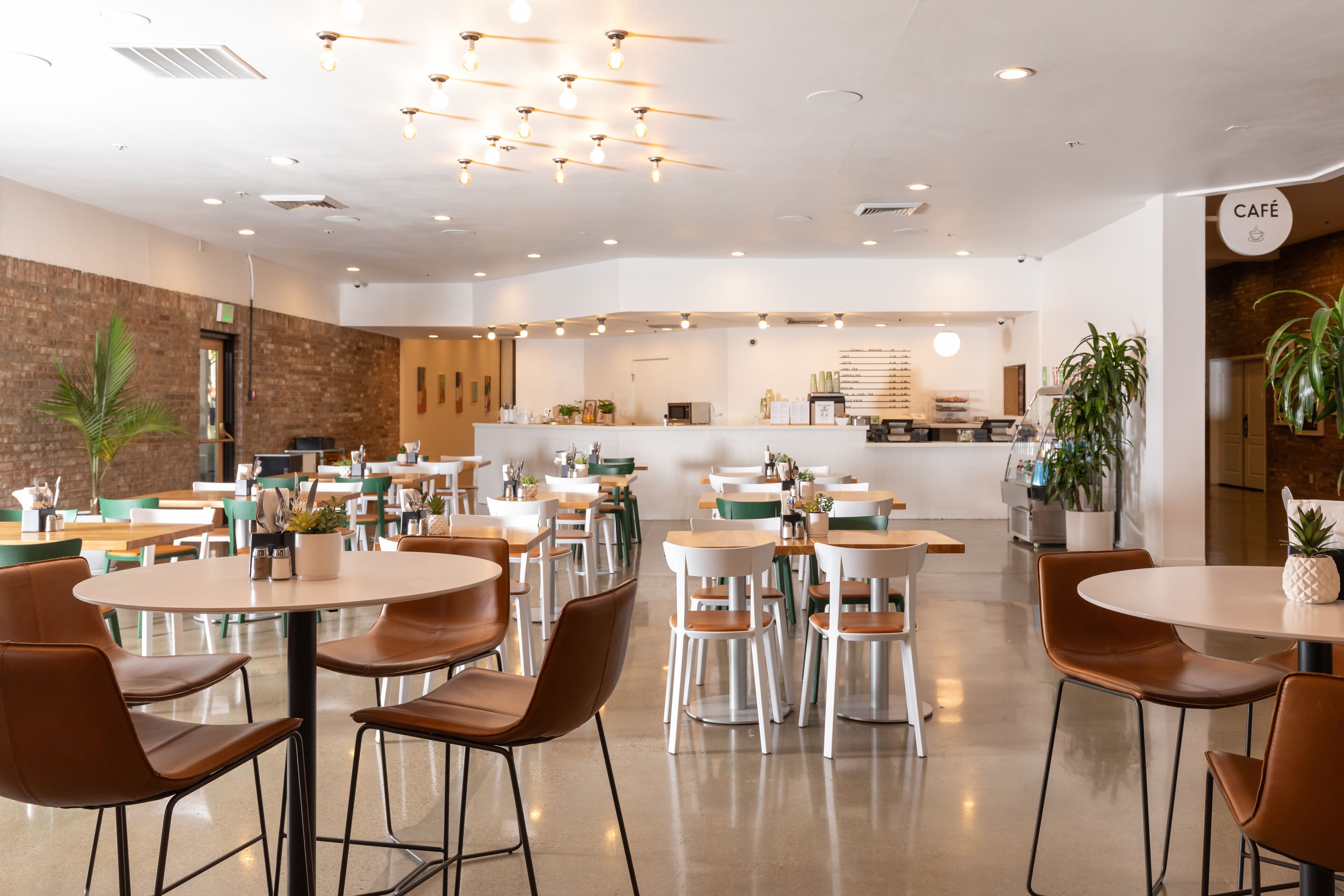 Un café moderno con mesas y sillas redondas, una pared de ladrillo y un letrero que dice "CAFÉ".
