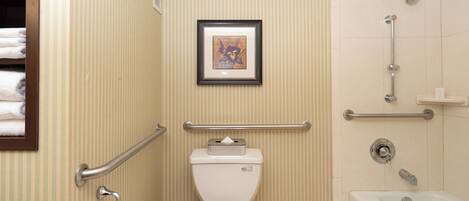 A bathroom with a toilet, a framed picture on the wall, a shower area with grab bars, and a bathtub.