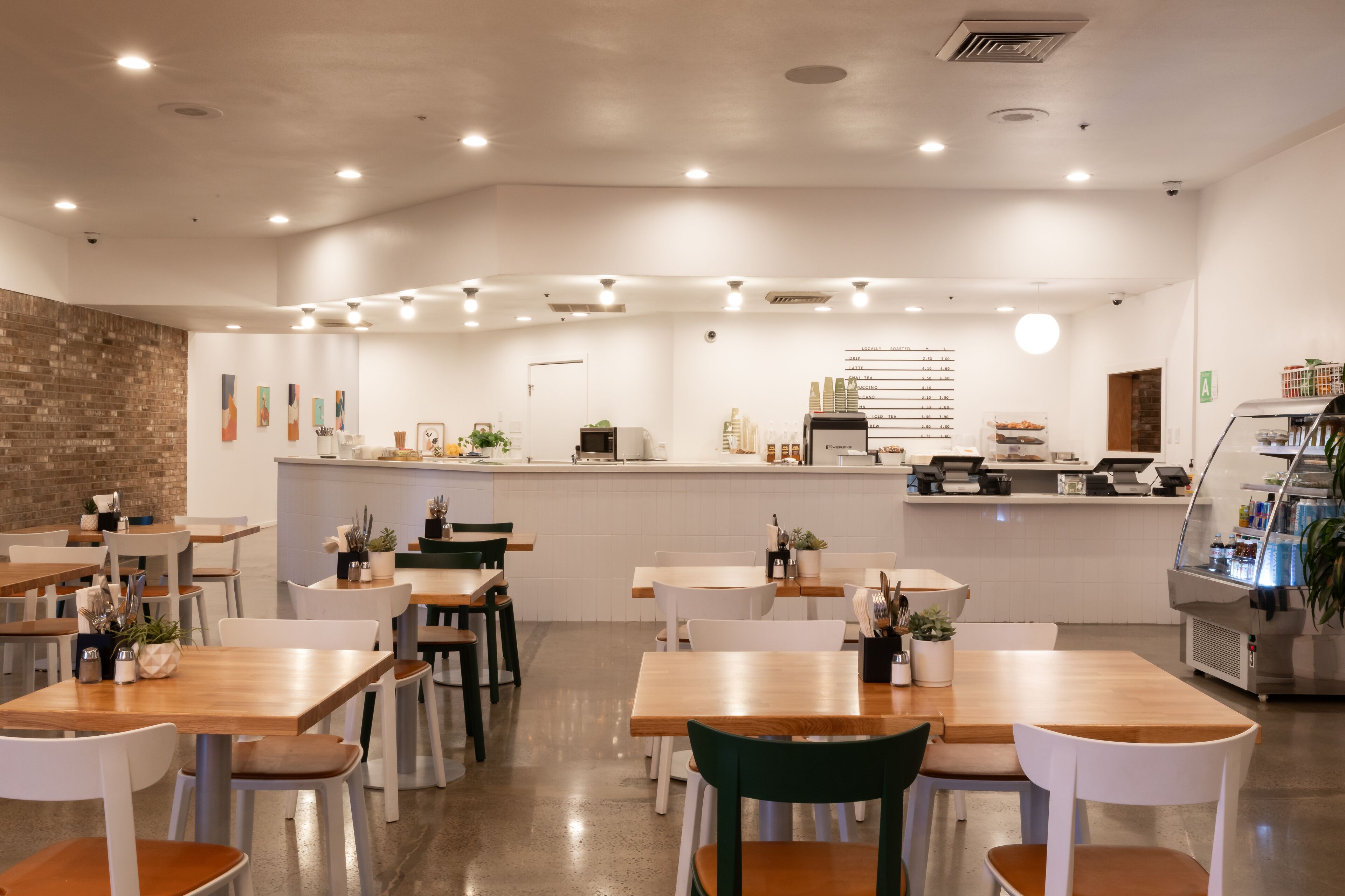 A modern restaurant interior with wooden tables, white chairs, and a central counter.
