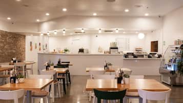Een modern restaurantinterieur met houten tafels, witte stoelen en een centrale bar.