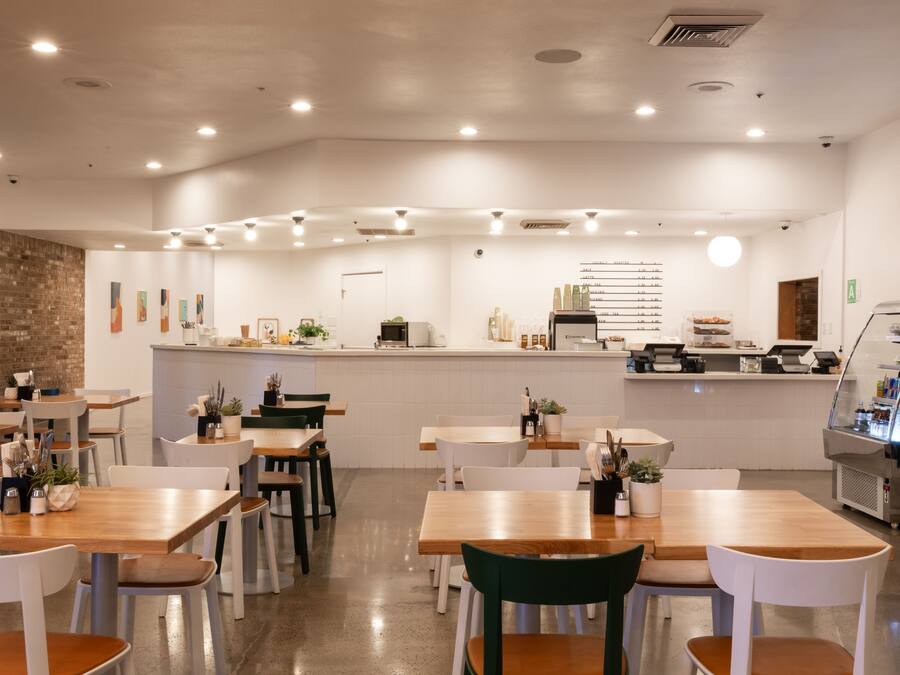 Een modern restaurantinterieur met houten tafels, witte stoelen en een centrale bar.