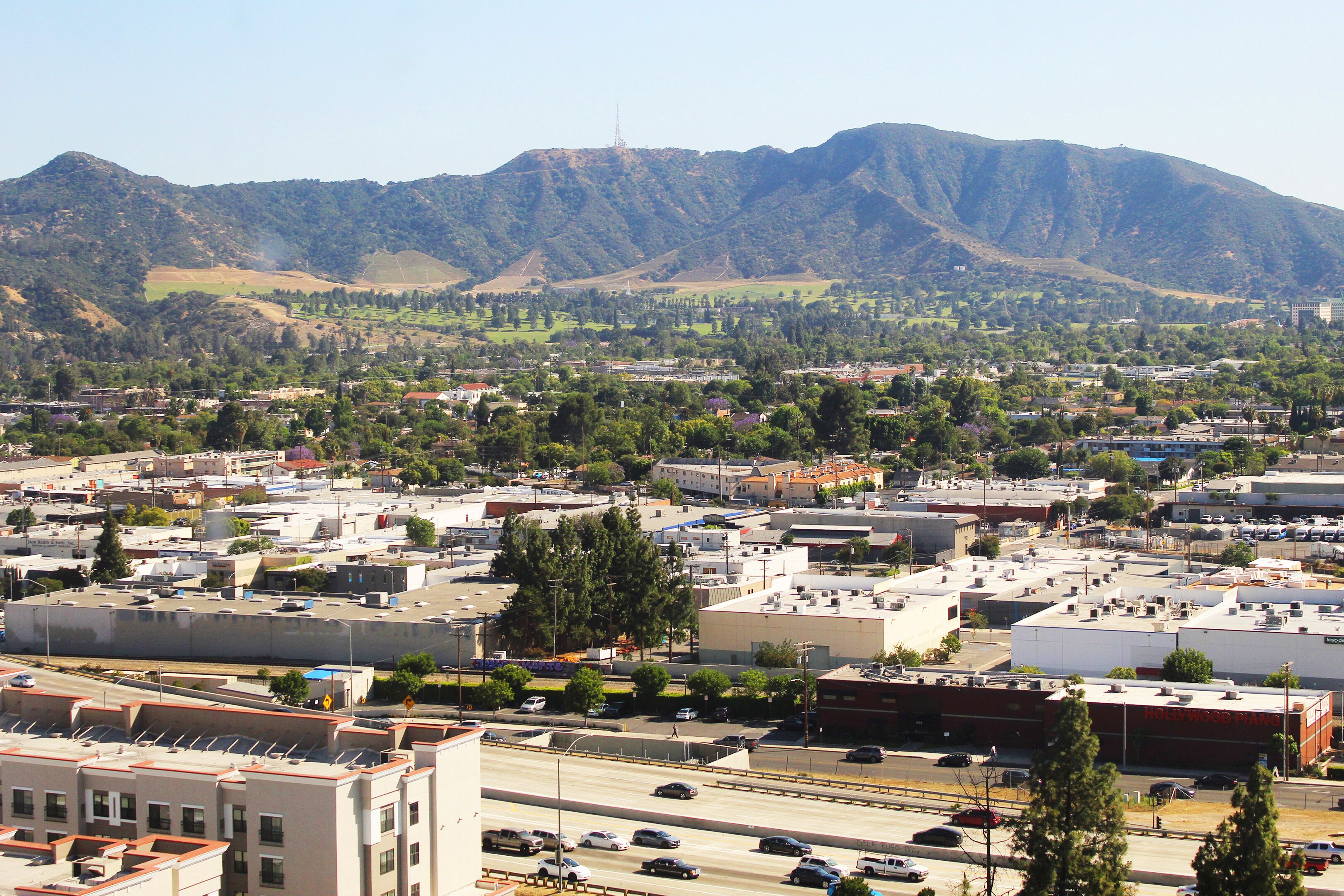A cityscape with a mountain range in the background, a highway with vehicles, and buildings with flat roofs.