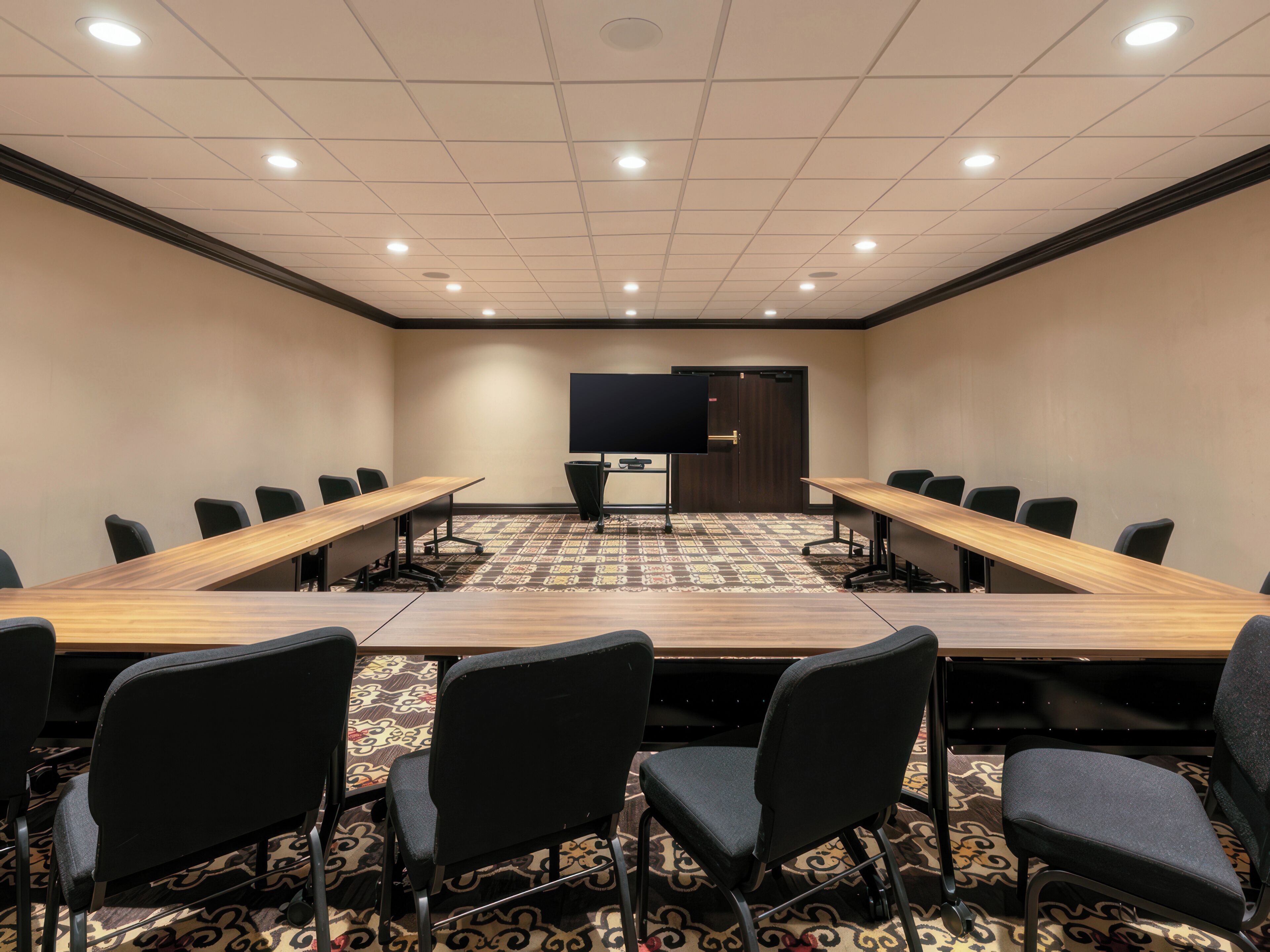 A conference room with a long table, chairs, a projector screen, and a door.