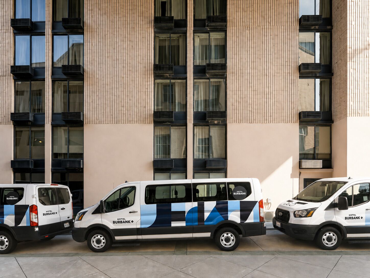 Three white vans parked in front of a building with vertical wooden paneling and large windows.