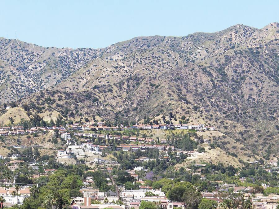 A residential area with houses on a hillside, surrounded by mountains.