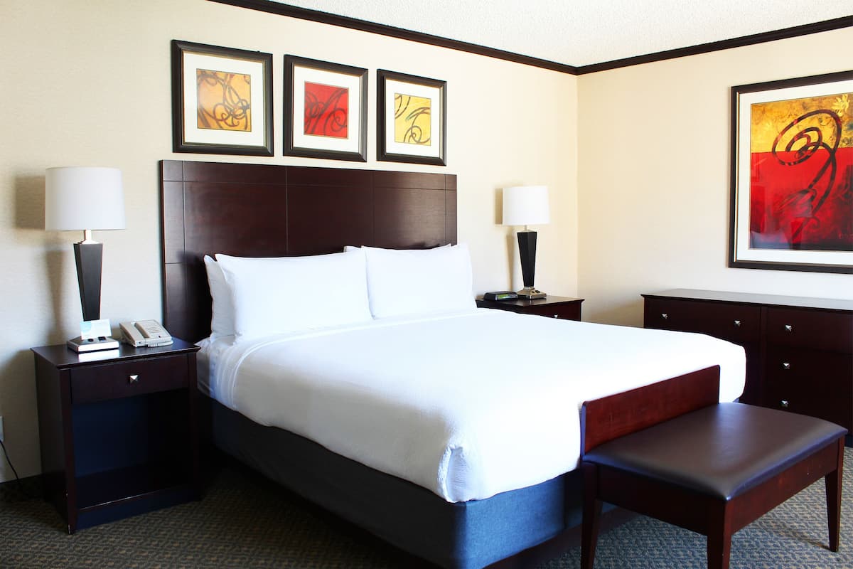 A hotel room with a large bed, two bedside tables, a bench, and three framed artworks on the wall.