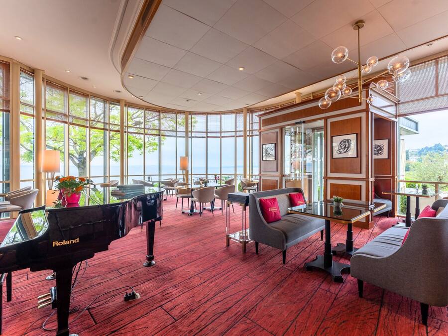 Un amplio vestíbulo de hotel con un piano de cola, asientos cómodos y grandes ventanales que ofrecen una vista panorámica.