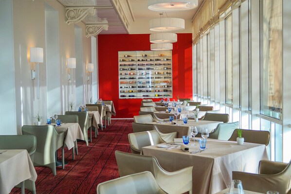 A restaurant with tables set for dining, a red accent wall, and a wine display.