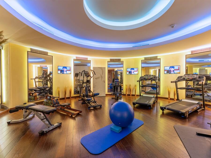 A modern gym with various exercise equipment, including treadmills, elliptical machines, and free weights, arranged in a spacious layout.