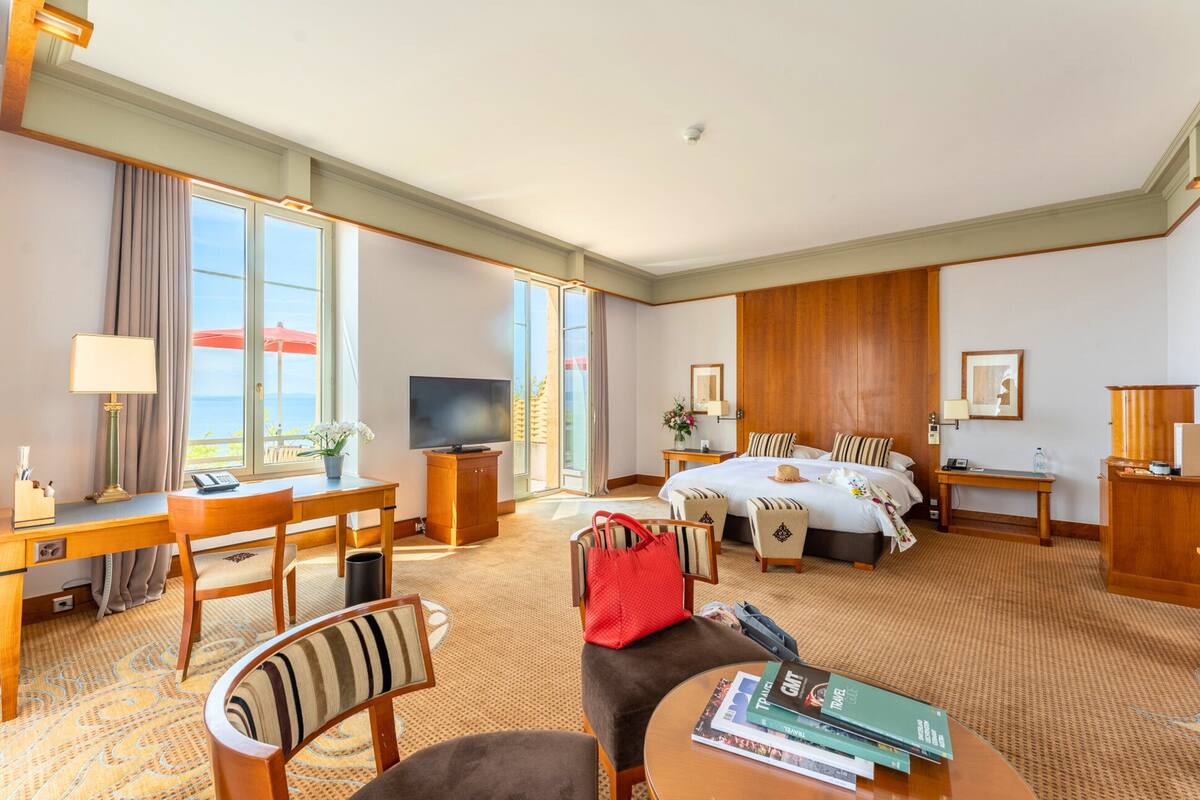 A hotel room with a large bed, a desk, a TV, a chair, a table, and a view of the outdoors.