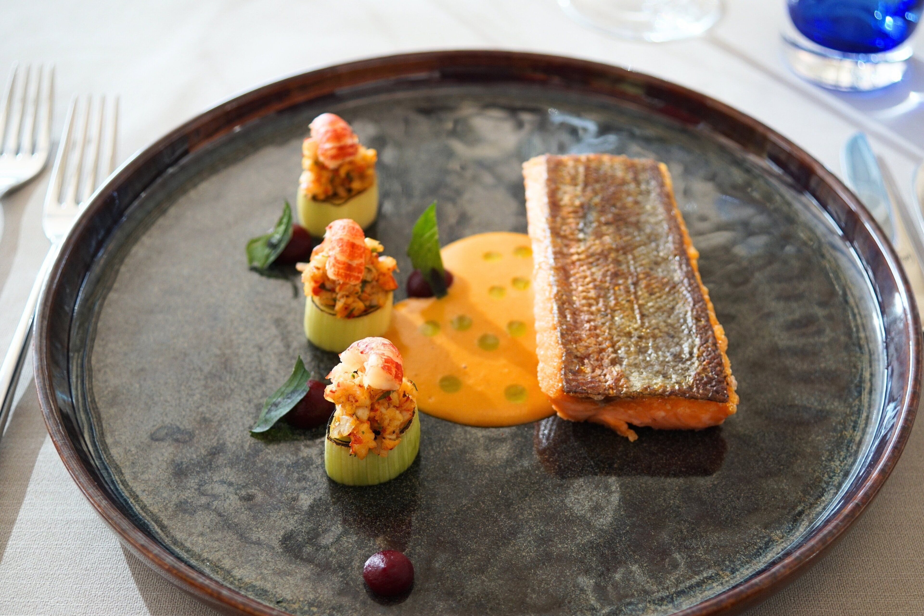 A plate with a piece of grilled fish, two stuffed vegetables, and a dollop of sauce.