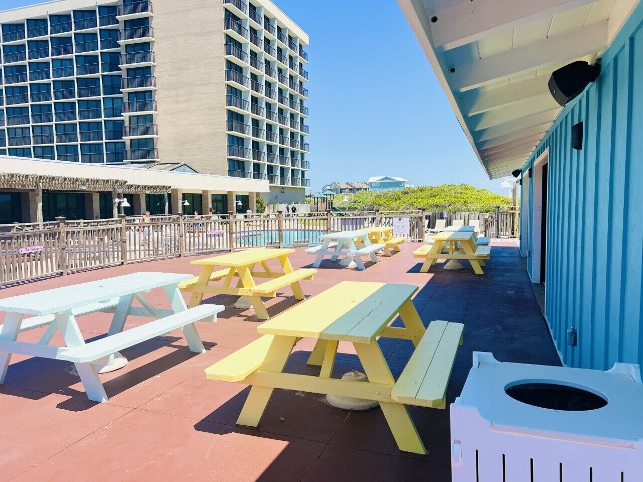 A rooftop patio with picnic tables and a trash bin, overlooking a cityscape.