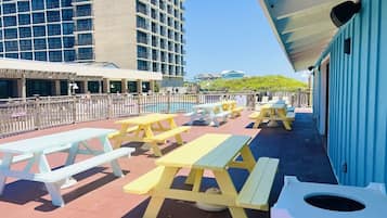 A rooftop patio with picnic tables and a trash bin, overlooking a cityscape.