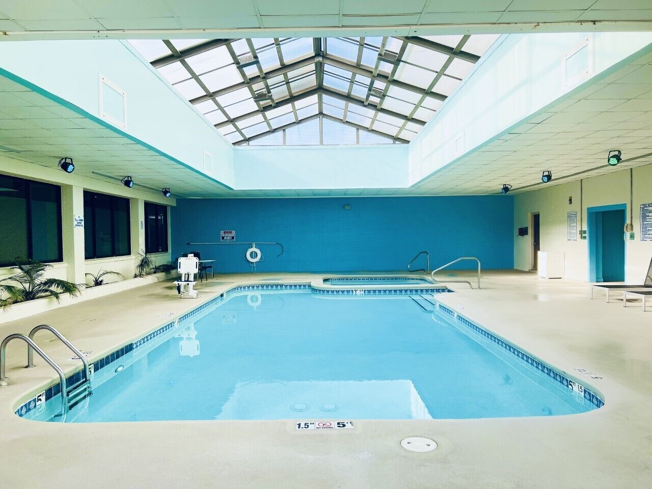 An indoor swimming pool with a skylight ceiling, clear water, and a lifeguard chair.