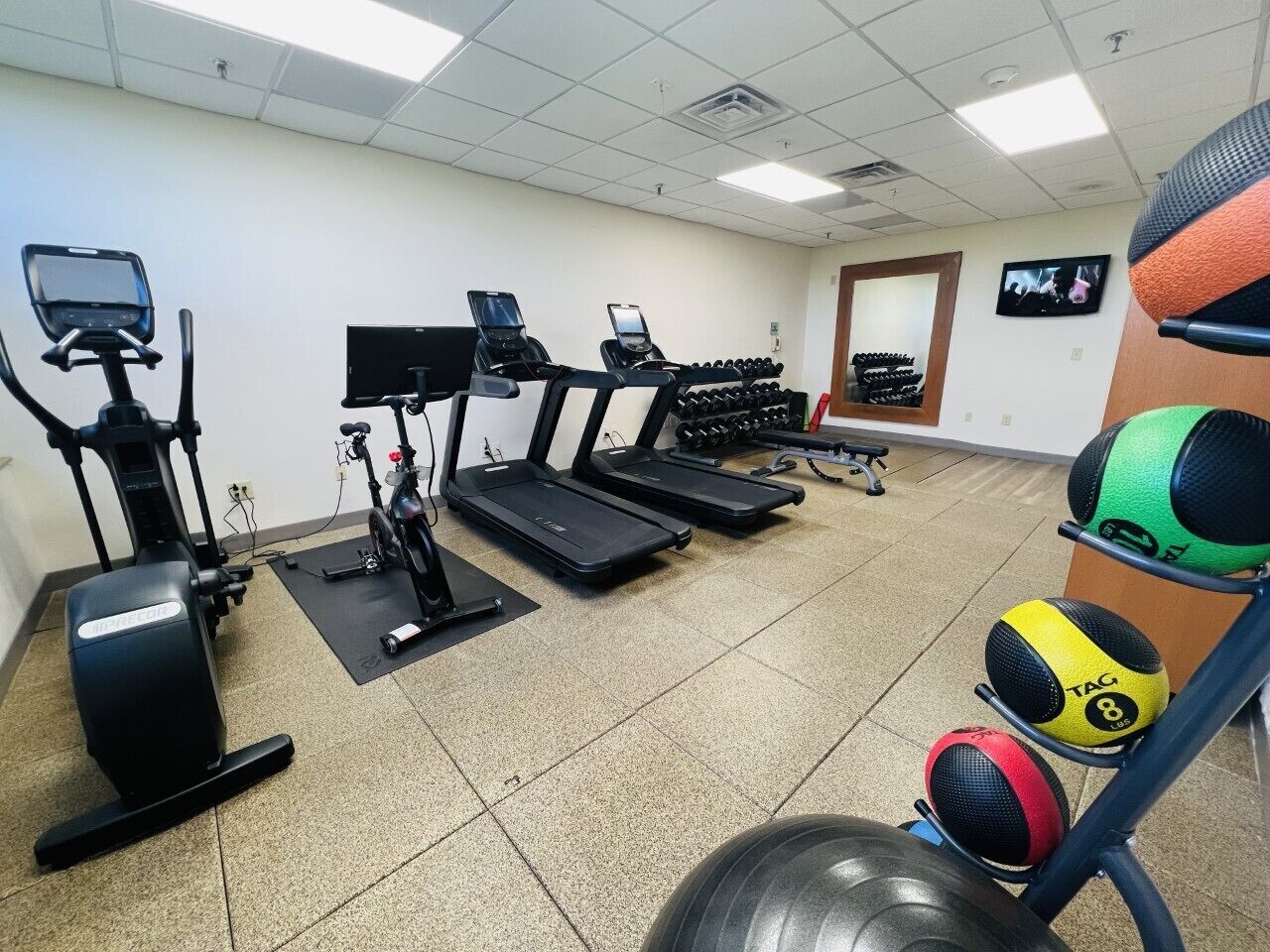 Un gimnasio con cintas de correr, elípticas y varios pesas.