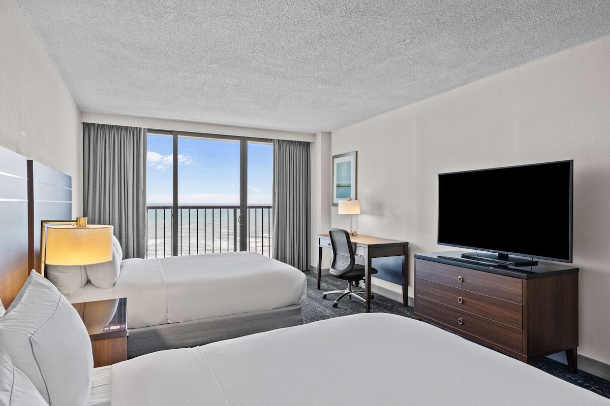 Habitación de hotel con dos camas, un escritorio, un televisor, una silla y una ventana con cortinas.