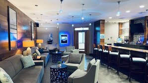 Un moderno vestíbulo de hotel con área de bar, arreglos de asientos y una pantalla de televisión.
