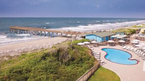 Un resort frente a la playa con un muelle, una piscina y sillas de playa.