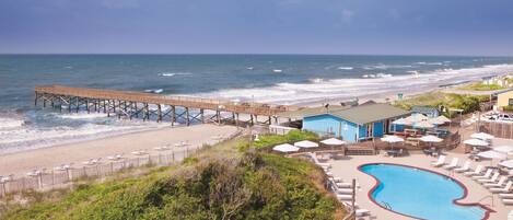 A beachside resort with a pier, a swimming pool, and beach chairs.
