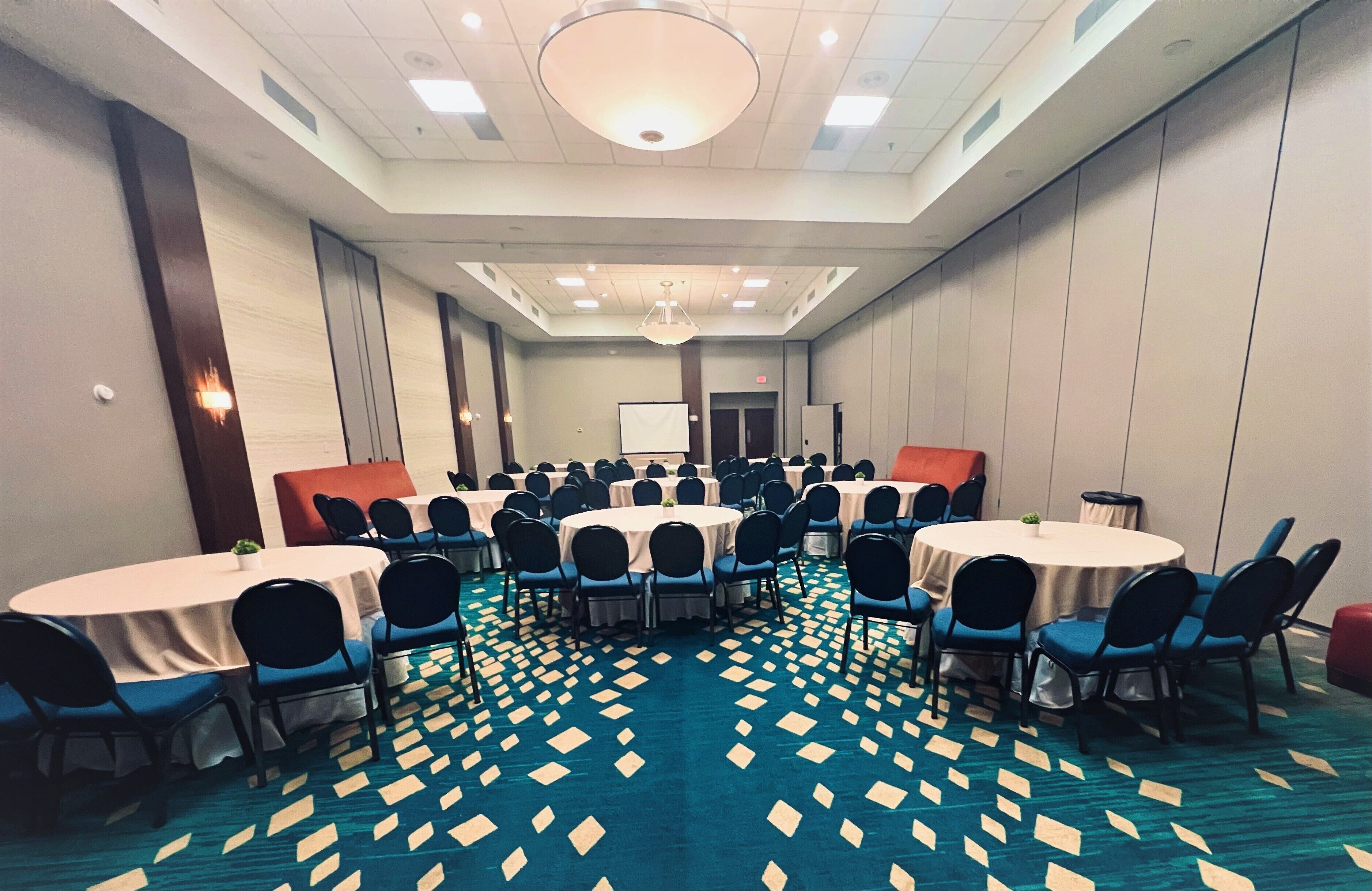A conference room with multiple round tables and chairs, a patterned carpet, and a large chandelier.