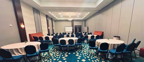 A conference room with multiple round tables and chairs, a patterned carpet, and a large chandelier.