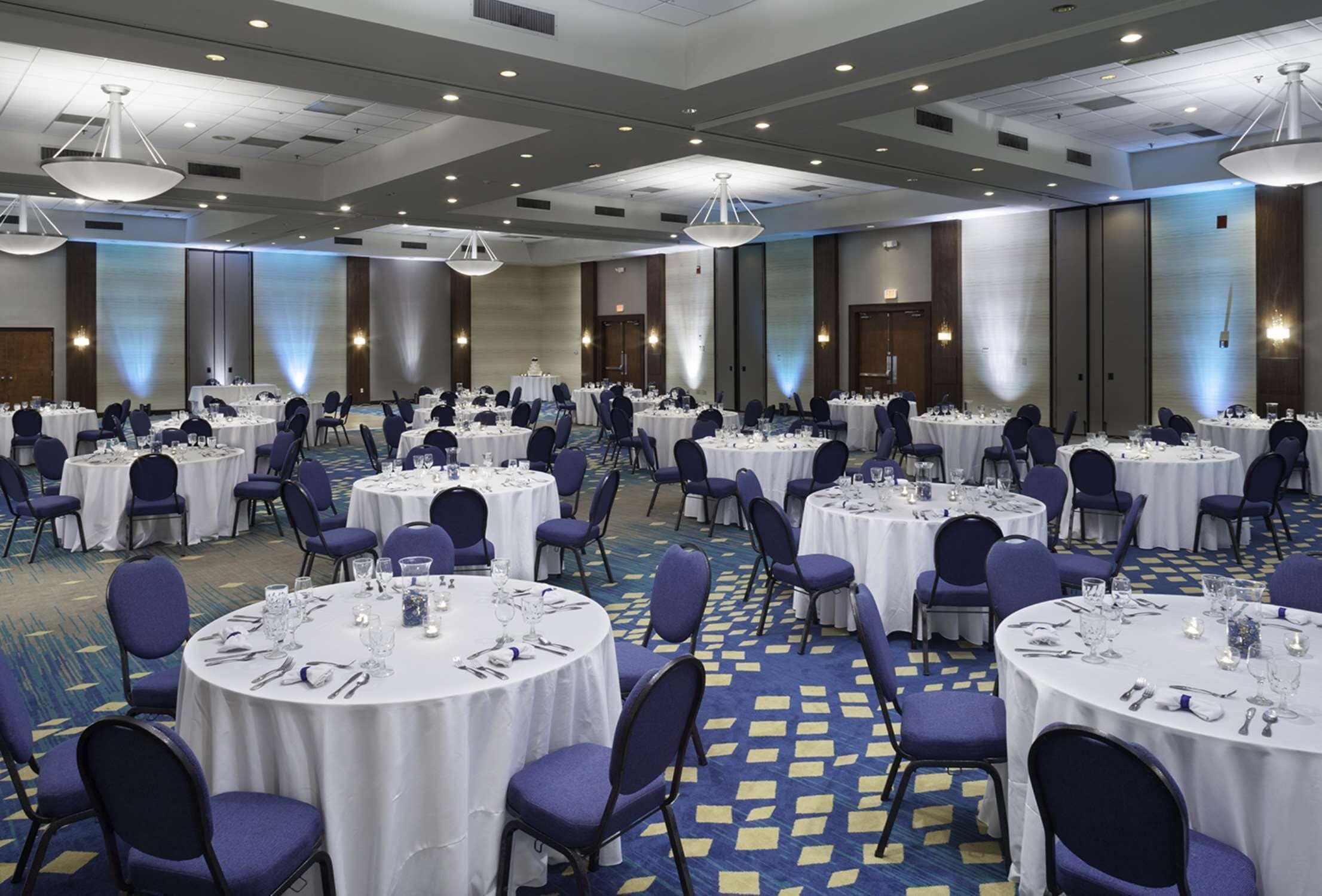 Une grande salle de banquet avec des tables rondes disposées pour le repas, équipées de chaises et de couverts.