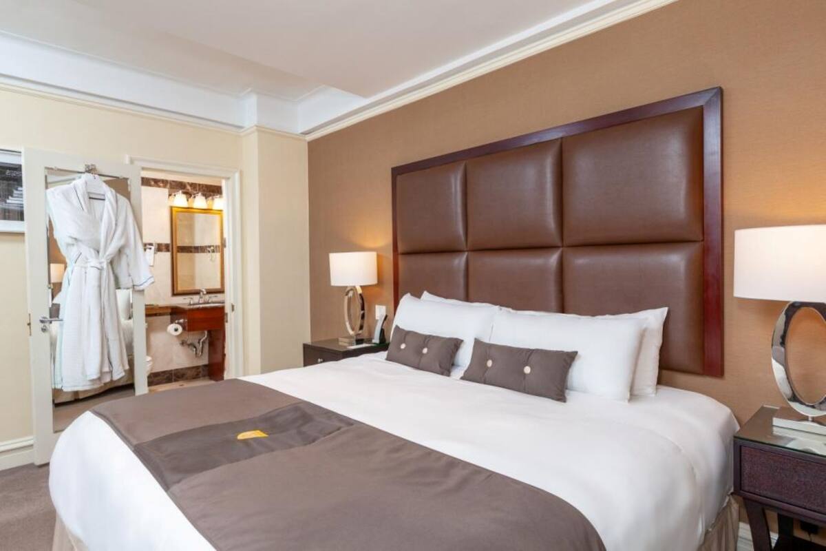A hotel room with a large bed, a wooden headboard, a bedside table with a lamp, and a robe hanging on a door.