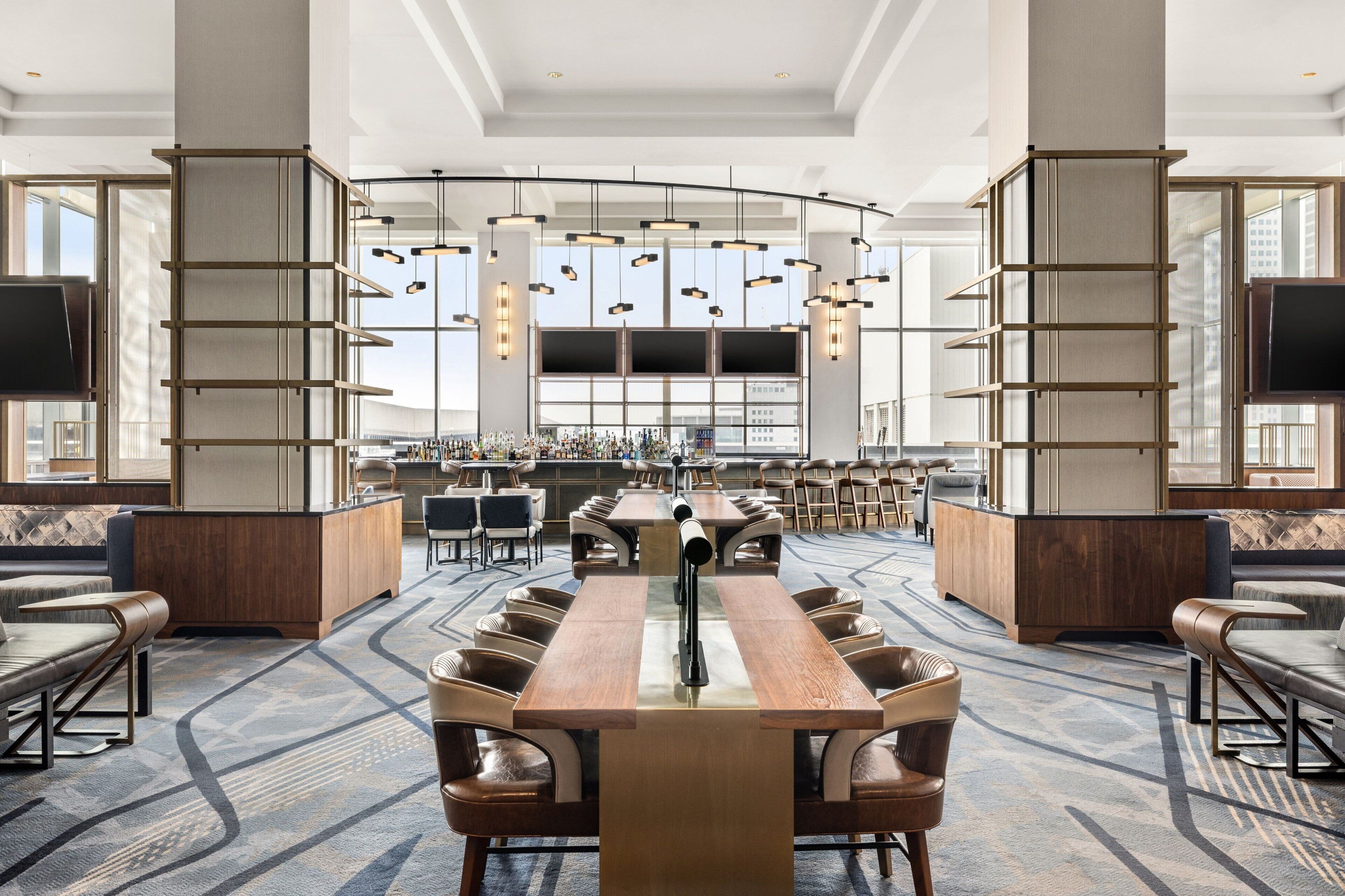 Un hall d’hôtel spacieux avec une longue table commune, des espaces aménagés pour s’asseoir et un bar.