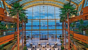 A spacious atrium with a glass ceiling, palm trees, and tables arranged for dining. - Detroit Marriott at the Renaissance Center (Detroit)