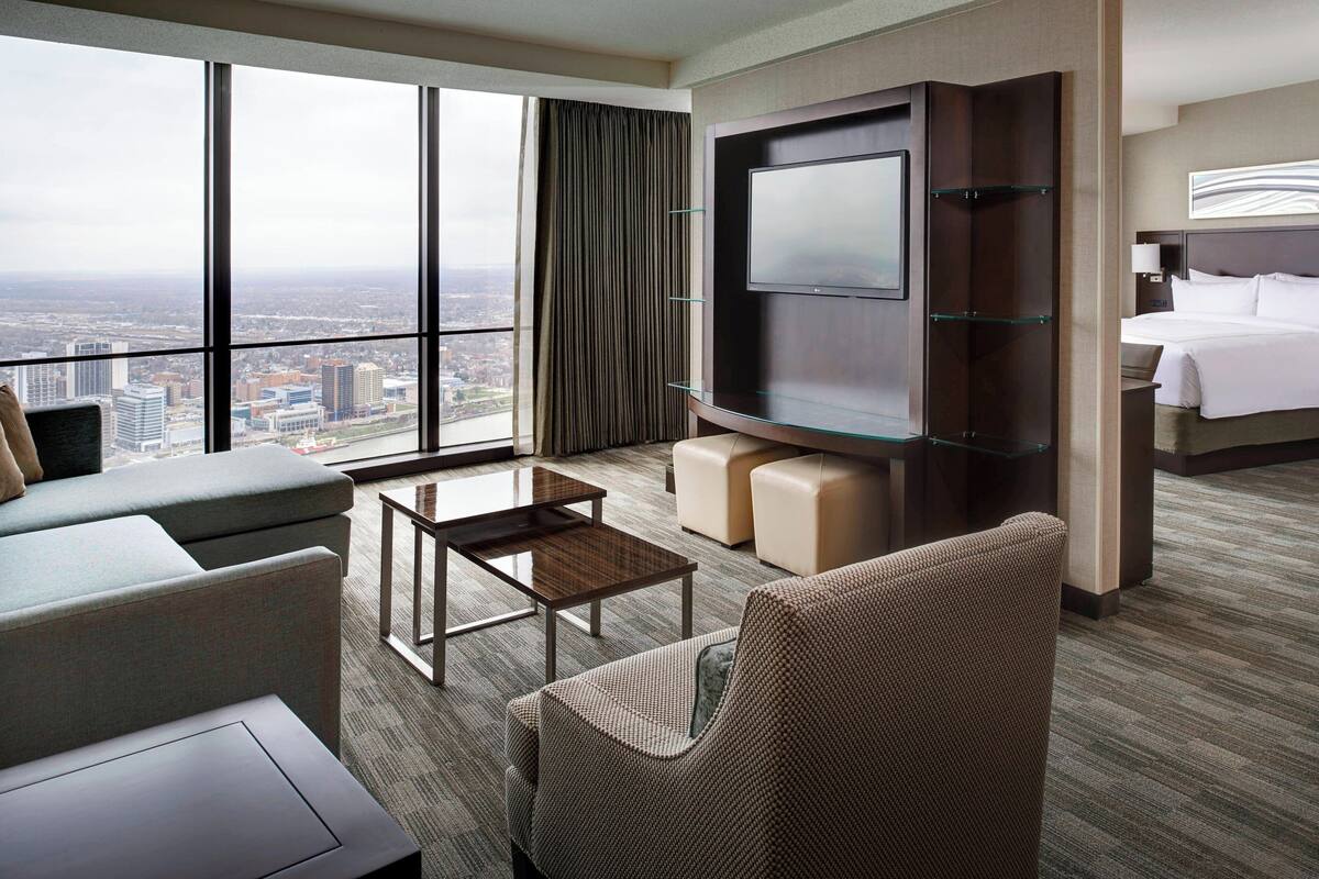 Una habitación de hotel con una televisión grande, un sofá, una silla, una mesa de centro y una cama.