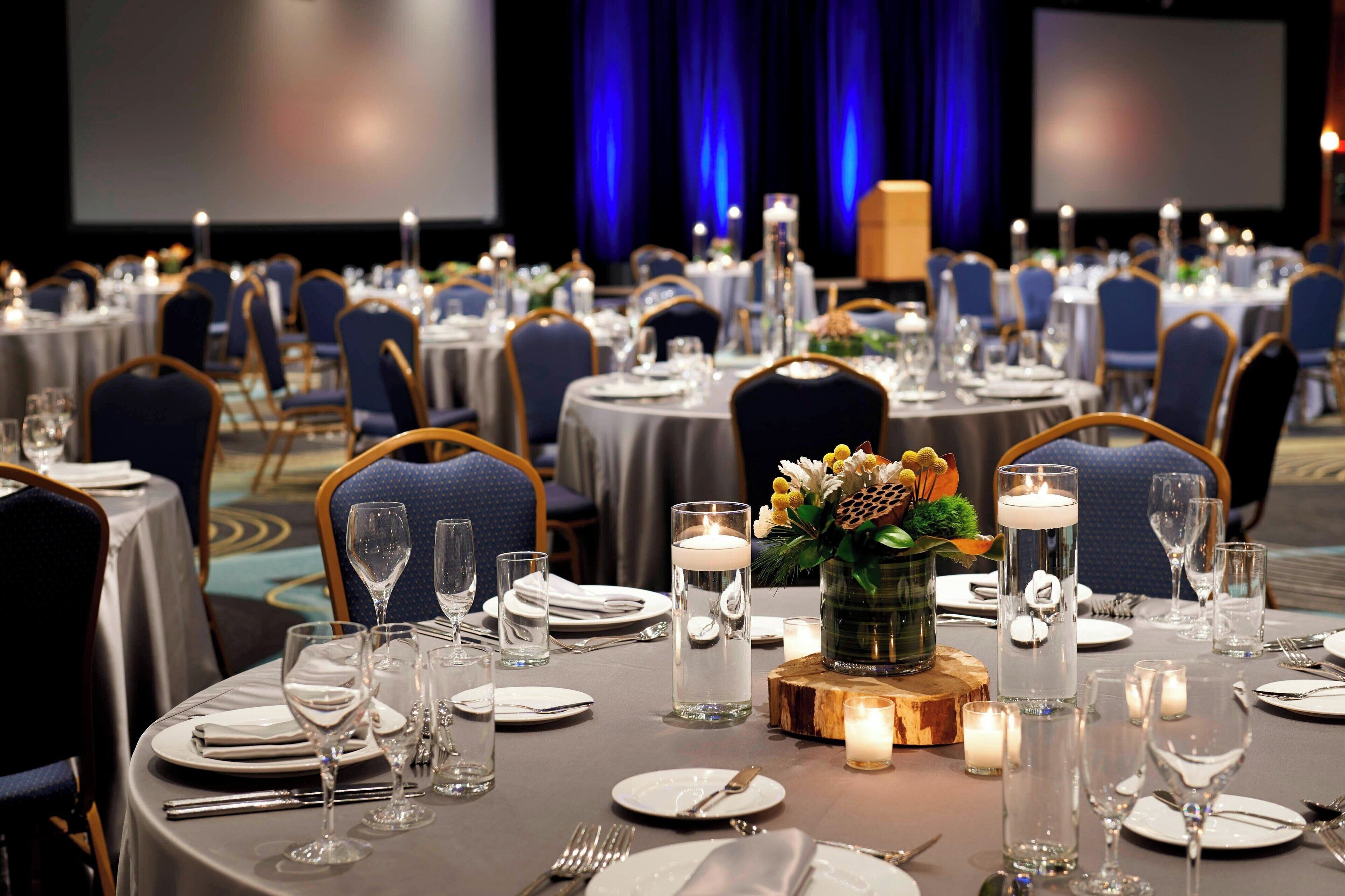 A banquet hall with round tables set for dining, featuring white tablecloths, candles, and floral centerpieces.