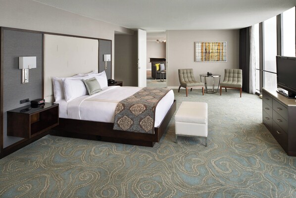 A hotel room with a large bed, a desk, a TV, and a seating area with two chairs.