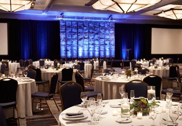 A banquet hall with round tables set for dining, chairs, and a large screen at the front.