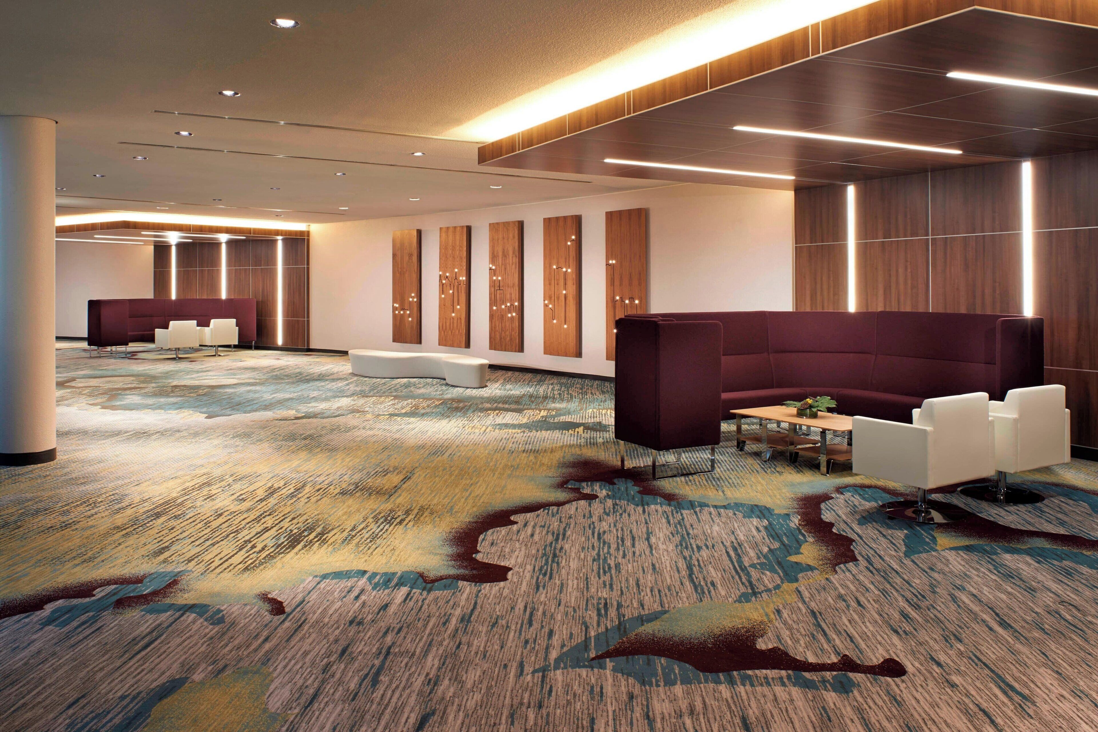 A modern hotel lobby with a large seating area, a reception desk, and a patterned carpet.