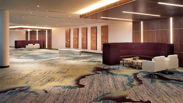 A modern hotel lobby with a large seating area, a reception desk, and a patterned carpet.