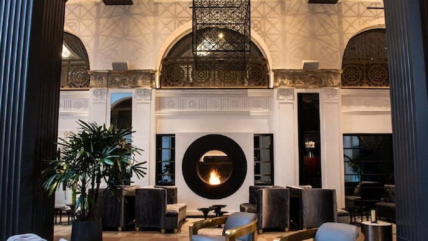 Un vestíbulo amplio con una chimenea circular central, un mobiliario elegante y una gran planta.