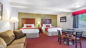 A hotel room with two beds, a sofa, a dining table with chairs, and a window with a view. - Baymont by Wyndham Bozeman (Bozeman)