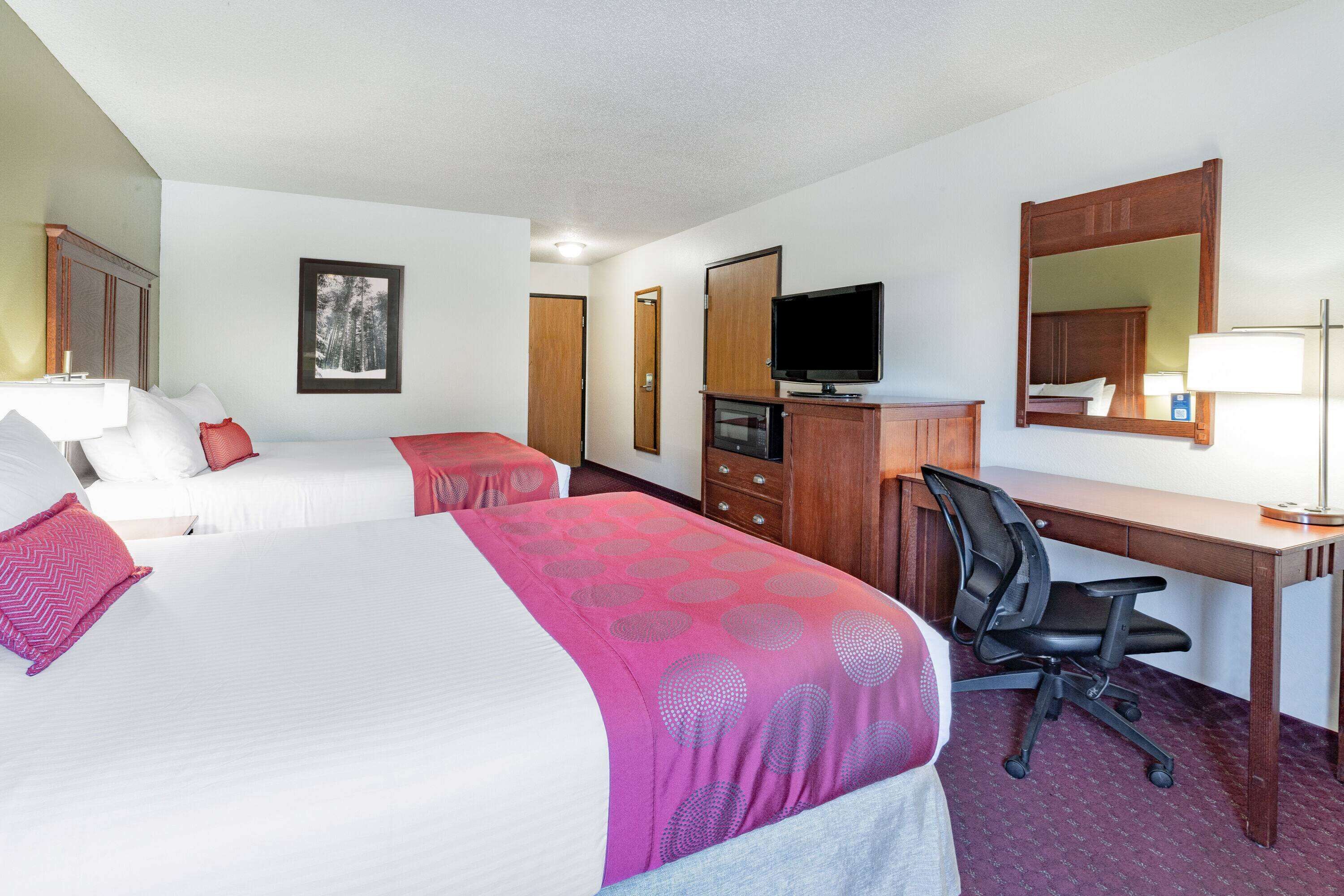 A hotel room with two beds, a desk, a chair, a television, and a mirror.