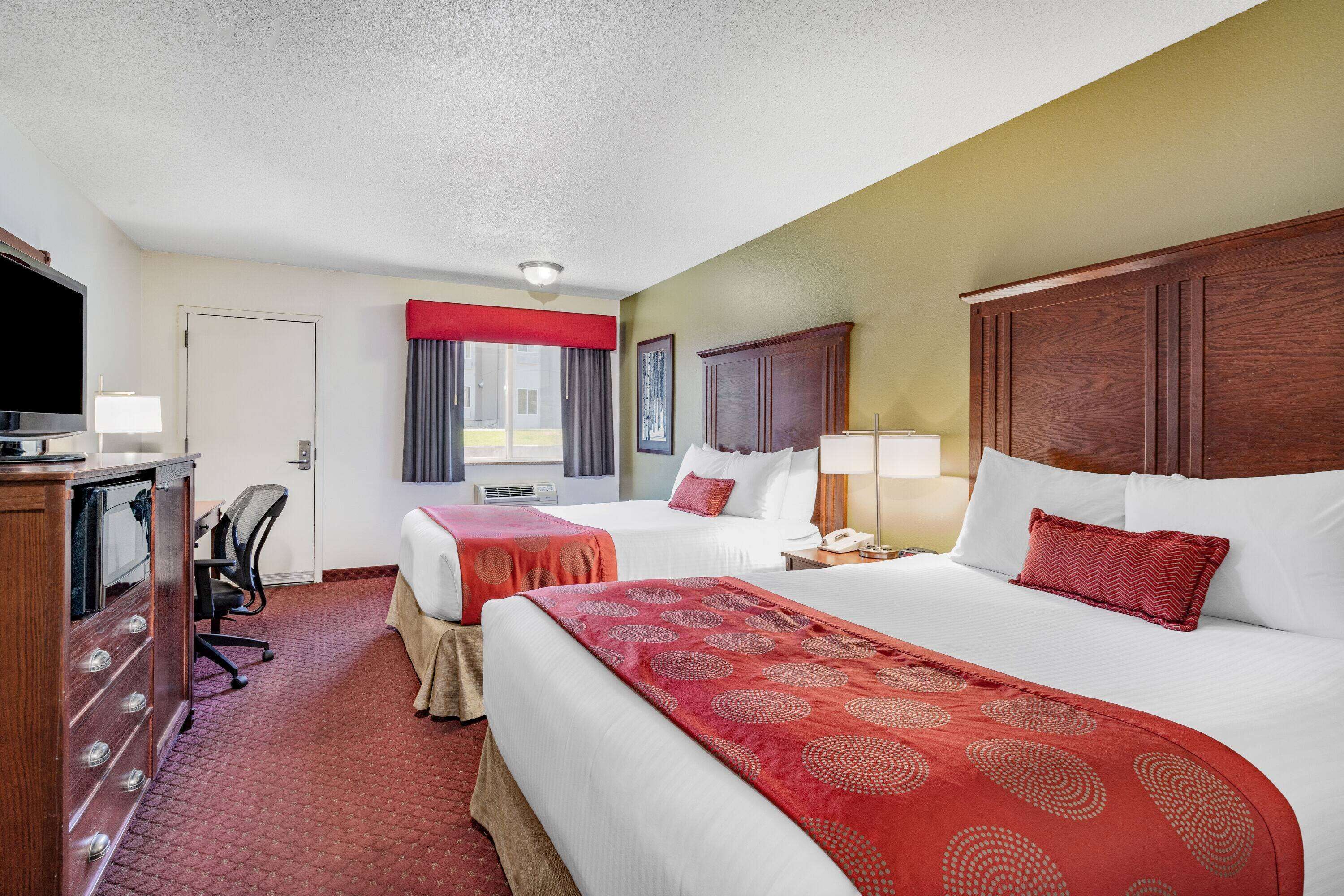 A hotel room with two beds, a desk with a TV, and a window with curtains.