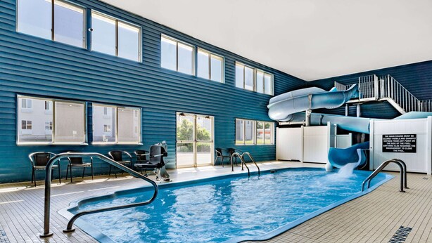 An indoor swimming pool with a slide, clear signage, and a view of the outside. - Baymont by Wyndham Bozeman (Bozeman)